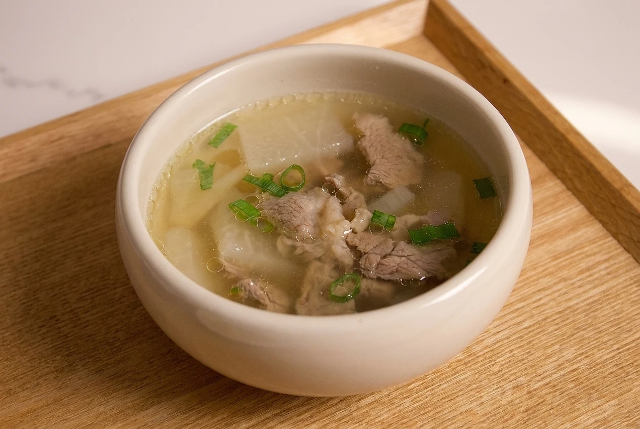 Korean beef and radish soup (sogogi muguk) with sliced beef, translucent radish, and chopped green onions in an ivory bowl on a wooden tray.